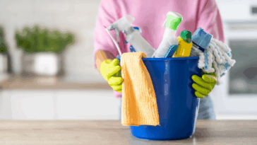A woman standing behind a bucket of cleaning supplies.
