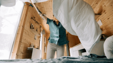A woman throwing a sheet over a bed.