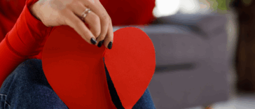 Woman holding up a paper heart that's been ripped in half