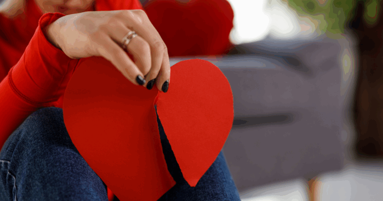Woman holding up a paper heart that's been ripped in half