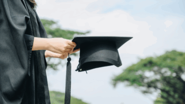 A woman in a. graduation gown holding a graduation cap.