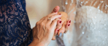 An older woman in an evening gown holding the hand of a bride.