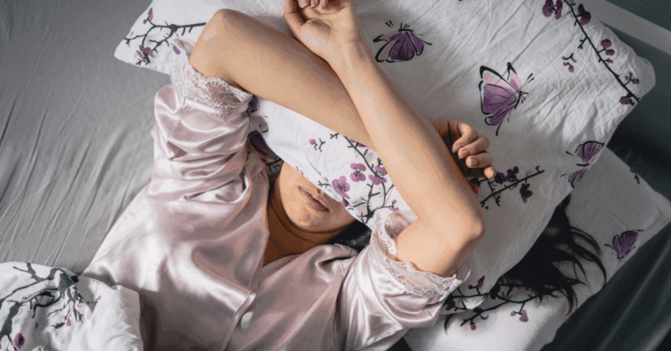 A woman lying in bed with a pillow covering her eyes.