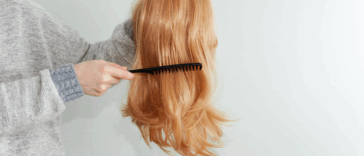 a woman combing a wig she's holding in her hand.