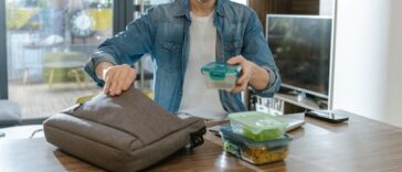 A man organizes lunch boxes while preparing for his day. The background shows a modern living space. This action emphasizes preparation, organization, and a healthy lifestyle.