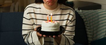 A sad woman in her 30s looking depressed and lonley while celebrating her birthday alone at home with a cake.