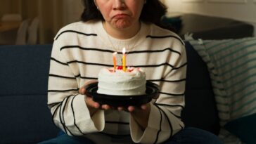 A sad woman in her 30s looking depressed and lonley while celebrating her birthday alone at home with a cake.