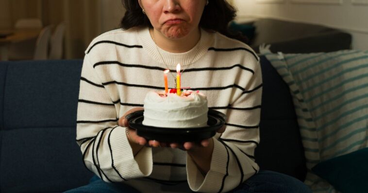 A sad woman in her 30s looking depressed and lonley while celebrating her birthday alone at home with a cake.