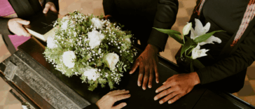 A group of people surrounding and laying their hands on a casket.