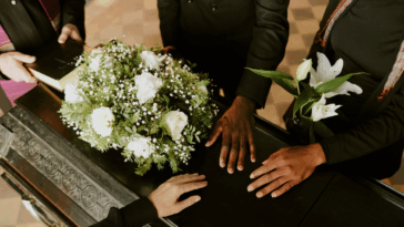 A group of people surrounding and laying their hands on a casket.