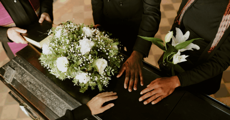 A group of people surrounding and laying their hands on a casket.
