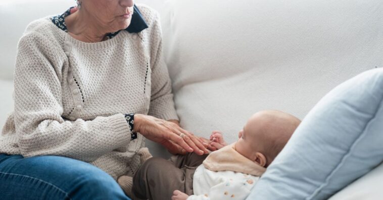 Grandmother caressing her newborn grandchild on the sofa: intergenerational connection and tender family moments.