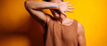 A man wearing a baseball cap covering his face with his arm.