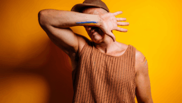 A man wearing a baseball cap covering his face with his arm.