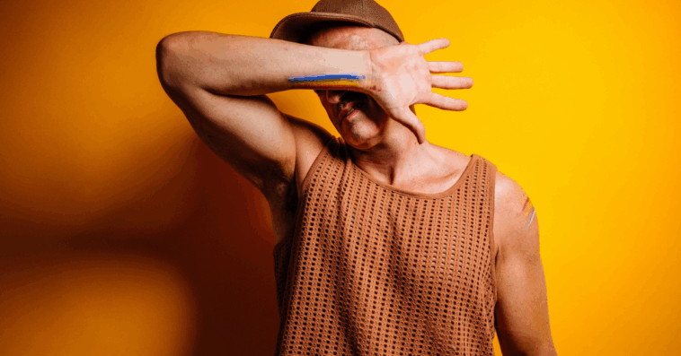 A man wearing a baseball cap covering his face with his arm.