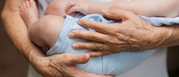 Cropped close-up photo of a baby boy sleeping in arms of a person.