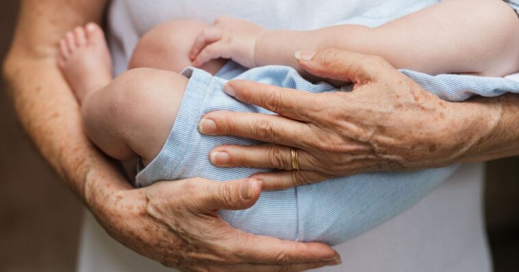 Cropped close-up photo of a baby boy sleeping in arms of a person.