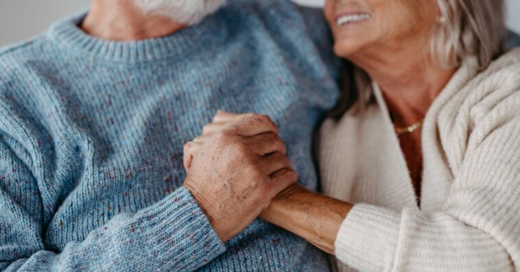 Close-up of senior couple cuddling and holding hands in their home.