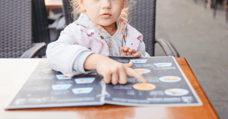 A Child sitting at a table looking at a menu.