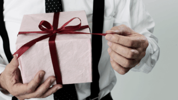 A man holding a present pulling on the ribbon.