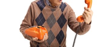Elderly man holding an old vintage rotary phone and looking at the handset isolated on white background.