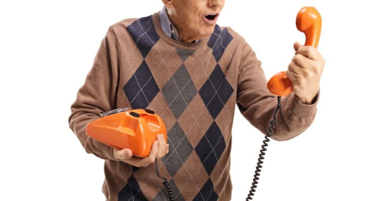 Elderly man holding an old vintage rotary phone and looking at the handset isolated on white background.