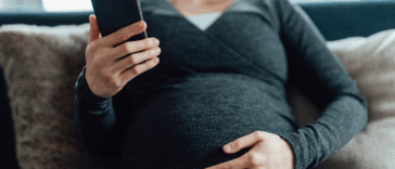 A pregnant woman sitting on the sofa looking at her phone.