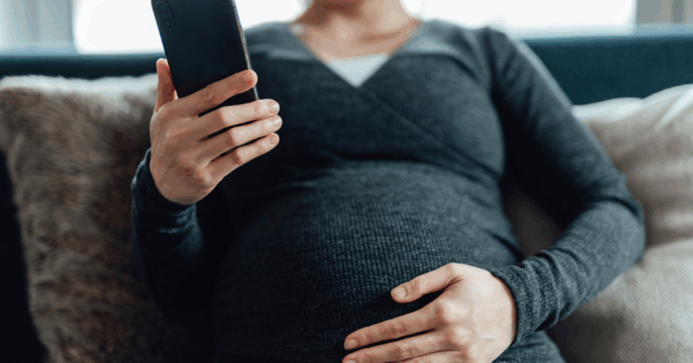 A pregnant woman sitting on the sofa looking at her phone.