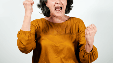 An older woman shaking her hands with her mouth open.