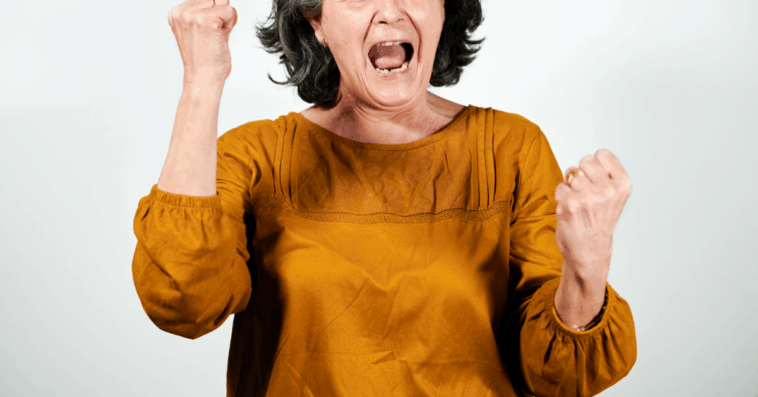 An older woman shaking her hands with her mouth open.