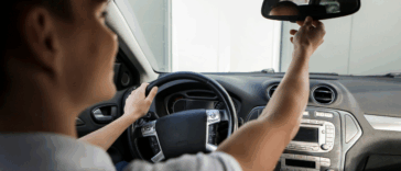 A teenager driving and adjusting their rearview mirror.