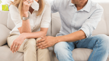 A woman sitting on the sofa crying with a man sitting next to her comforting her.
