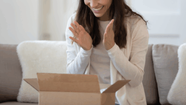 A woman sitting in front of an open cardboard box.