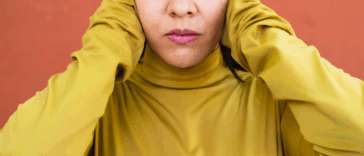 A woman in a yellow shirt covering her ears.