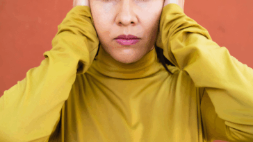 A woman in a yellow shirt covering her ears.