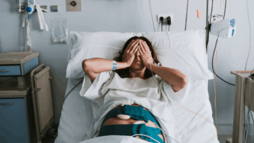 A woman in a hospital bed with her hands over her eyes.
