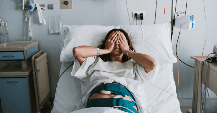 A woman in a hospital bed with her hands over her eyes.