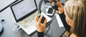 A woman with headphones in her hand looking at a computer.
