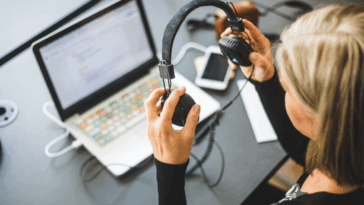 A woman with headphones in her hand looking at a computer.