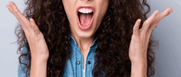 A woman with dark curly hair screaming with her hands in the air.