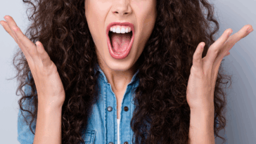 A woman with dark curly hair screaming with her hands in the air.