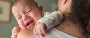 Baby with eyes closed screaming and crying on their mother's shoulder.