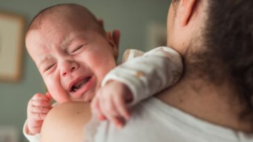 Baby with eyes closed screaming and crying on their mother's shoulder.