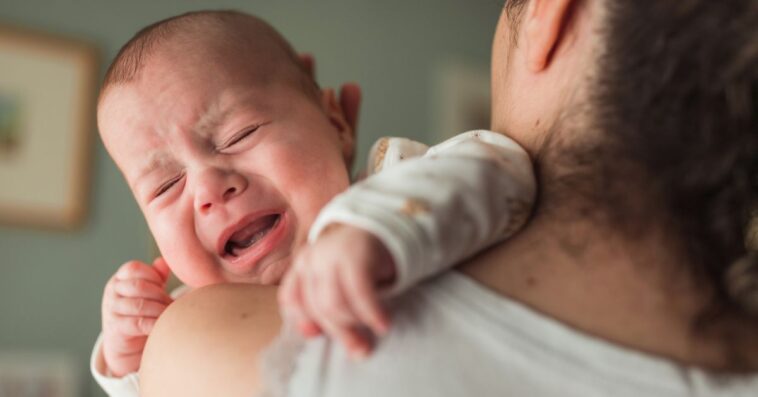 Baby with eyes closed screaming and crying on their mother's shoulder.
