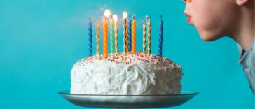 Boy blowing out candles on a birthday cake against blue background.