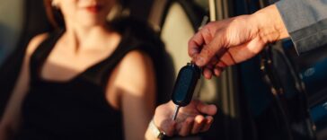 Closeup of a young woman receiving car keys from a sales representative showcasing automotive transactions or rental services in a covered parking environment.