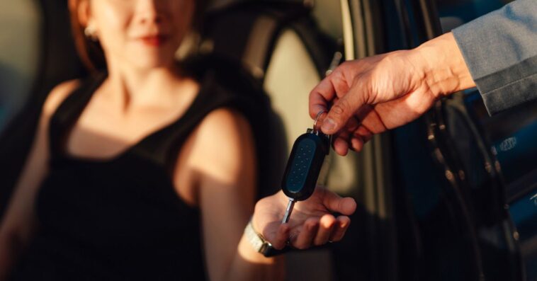 Closeup of a young woman receiving car keys from a sales representative showcasing automotive transactions or rental services in a covered parking environment.