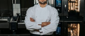 Portrait of confident, young male chef wearing a white uniform and standing with his arms crossed in the kitchen of a restaurant.