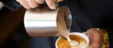 Barista hands pouring milk foam into of espresso resulting a pattern design on the surface of latte, Pouring Latte Art.