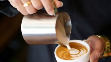 Barista hands pouring milk foam into of espresso resulting a pattern design on the surface of latte, Pouring Latte Art.